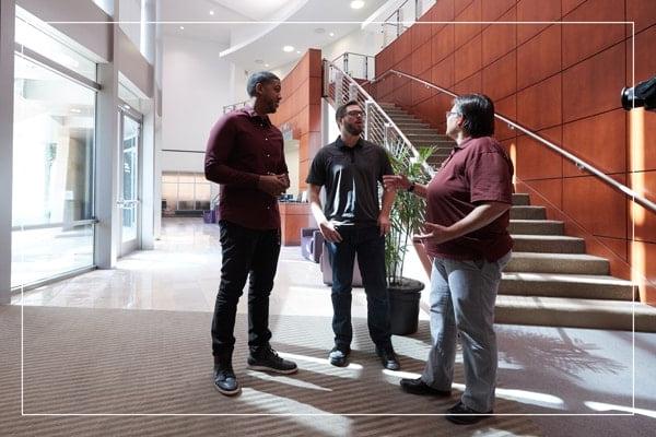 Faculty member speaking with two students in a hallway